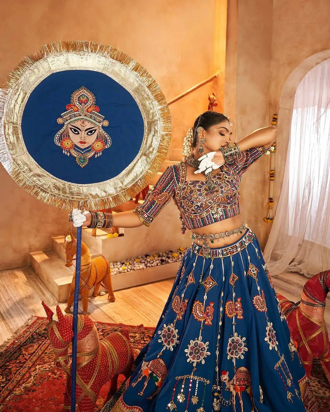 Woman in traditional outfit holding a decorative mirror with an embroidered design.